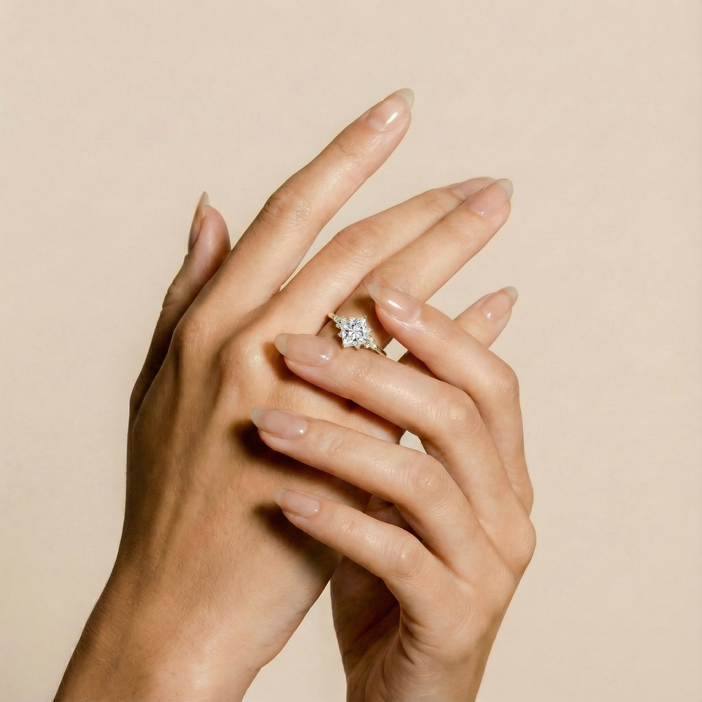 Hands with manicured nails wearing a diamond engagement ring against a neutral background