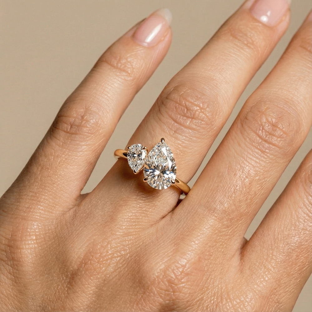 Hand wearing a gold ring with two pear-shaped diamonds