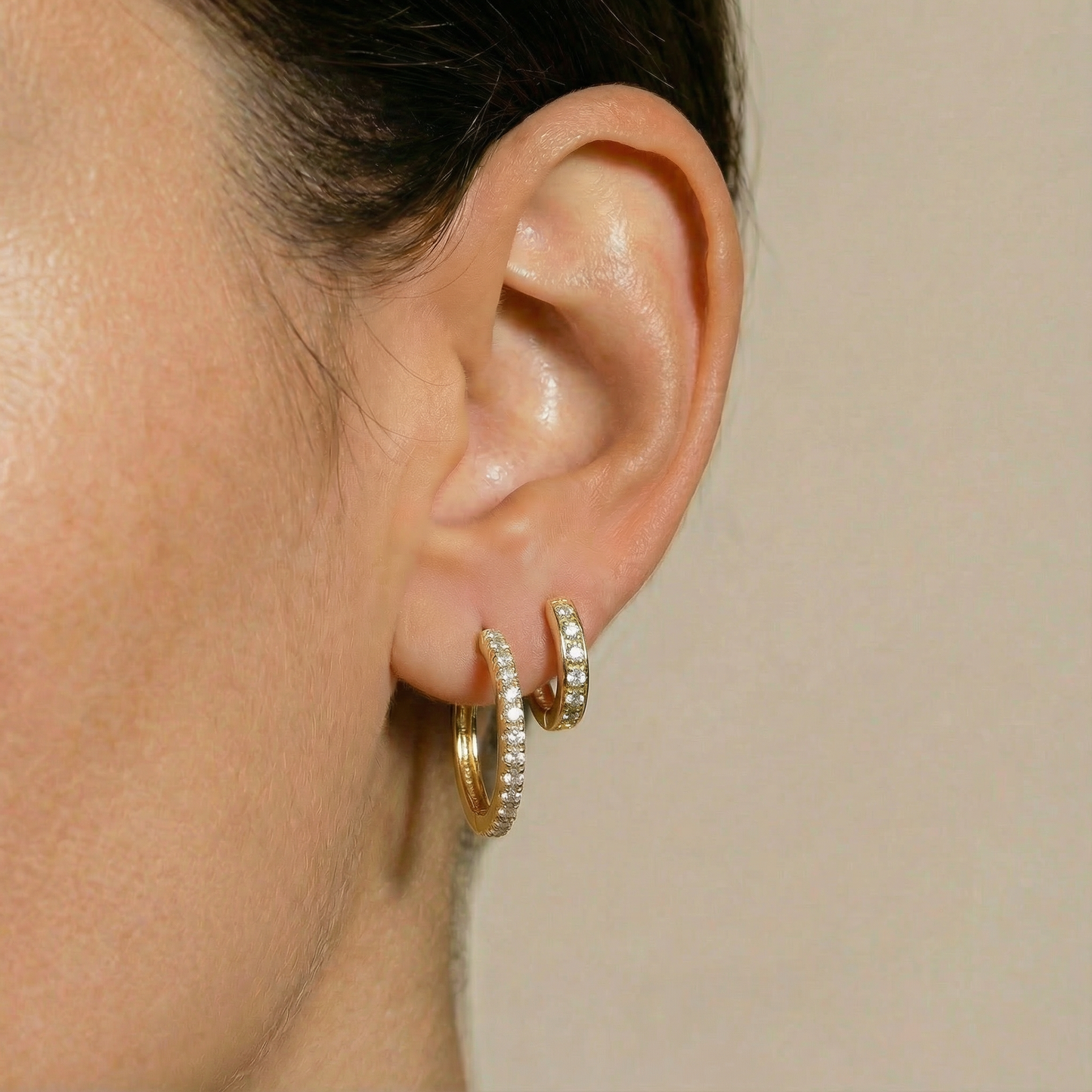 
                  
                    Close-up of an ear wearing 18ct gold hoop Solene and Solene Mini huggie Earrings by Karat Goldsmiths 
                  
                
